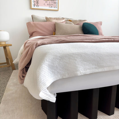 Close-up of Yona Cardboard Bed in black finish with textured white bedding and pastel pillows