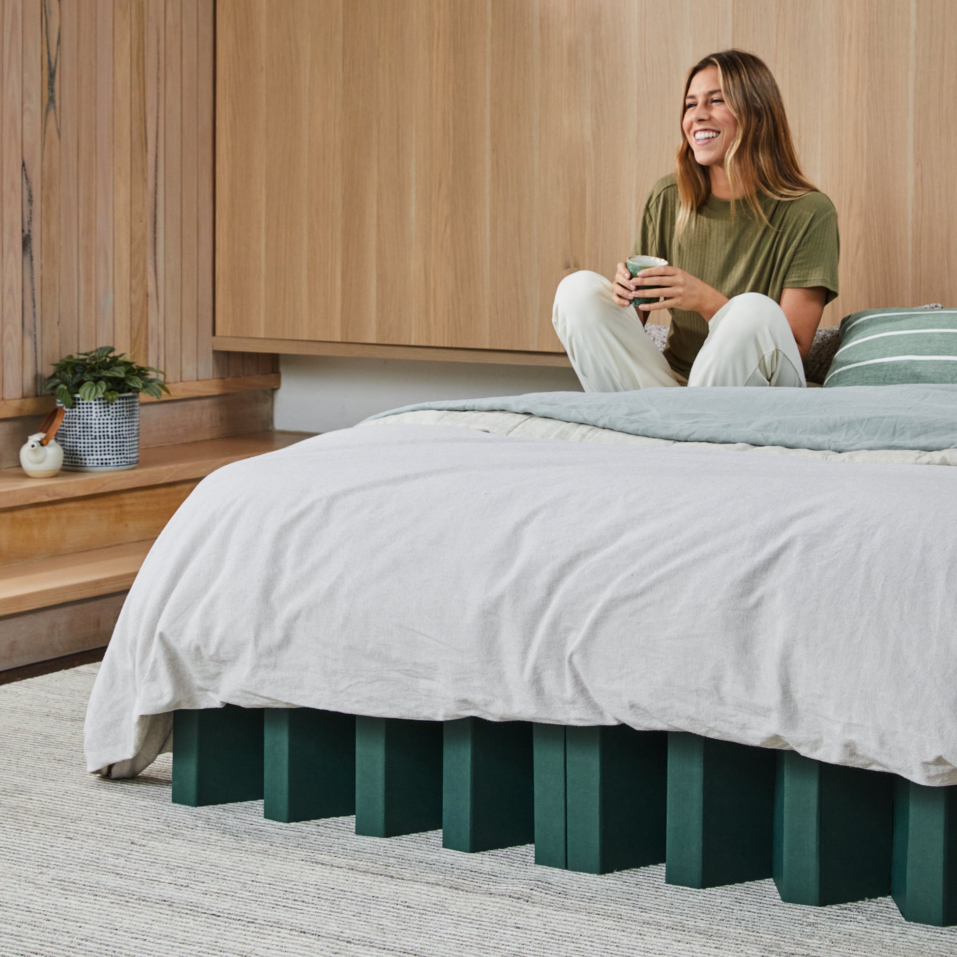 Yona Cardboard Bed in forest green finish with soft bedding and a person relaxing in a cozy bedroom